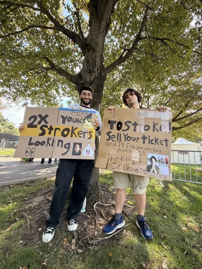 Artem Sumin and a friend holding handmade signs asking for Strokes tickets outside a concert